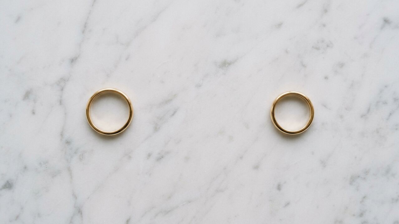 Two plain gold wedding bands placed apart on marble — symbolic of mutual divorce
